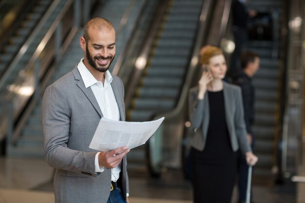 Homme d'affaires souriant debout dans la zone d'attente, lisant le journal