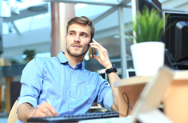 Homme d'affaires souriant debout et utilisant un téléphone portable au bureau