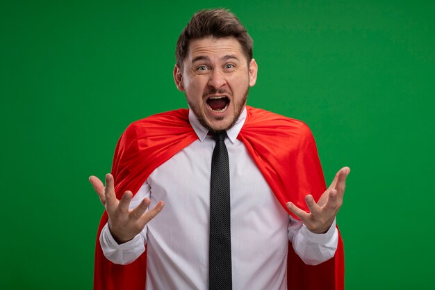 Homme d'affaires de super héros en cape rouge criant avec les bras levés avec une expression agressive debout sur le mur vert