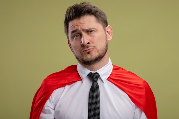 Photo gratuite homme d'affaires de super héros en cape rouge lookign à la caméra avec une expression triste sur le visage debout sur fond vert