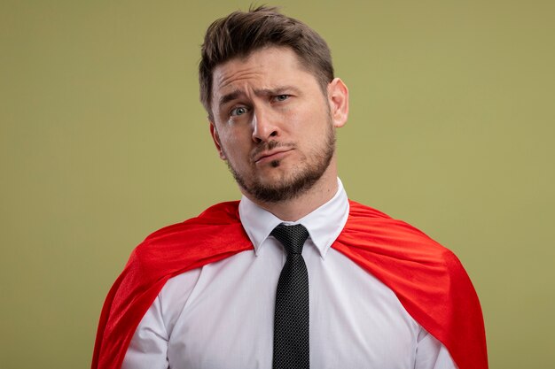 Homme d'affaires de super héros en cape rouge lookign à la caméra avec une expression triste sur le visage debout sur fond vert