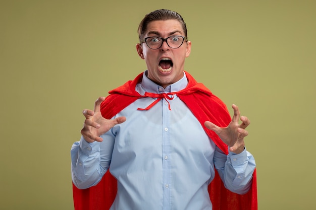 Homme d'affaires de super héros en cape rouge et lunettes criant avec les mains levées fou fou devenir sauvage debout sur fond clair