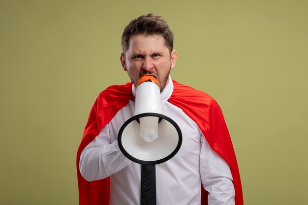 Homme d'affaires de super héros en colère en cape rouge criant au mégaphone avec une expression agressive debout sur fond vert