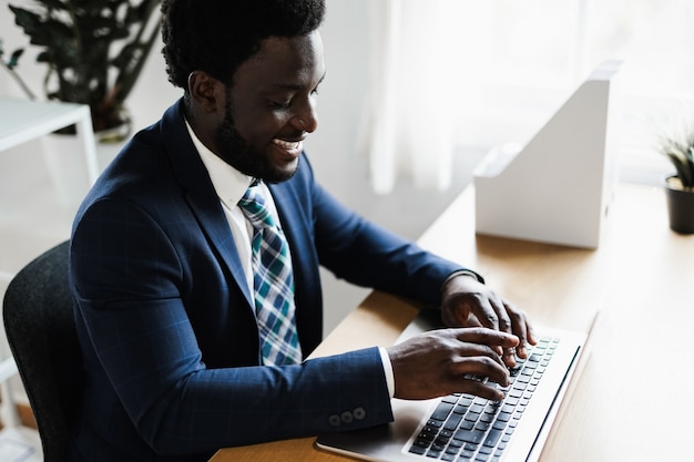 Homme africain d'affaires travaillant à l'intérieur d'un bureau moderne à l'aide d'un ordinateur portable - focus on face