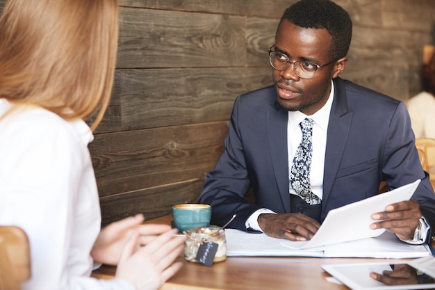 Homme africain confiant en tenue de soirée tenant CV, écoutant attentivement la femme rousse