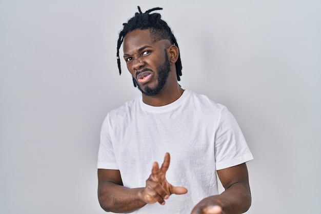 Homme africain avec des dreadlocks portant un t-shirt décontracté sur fond blanc expression dégoûtée mécontent et effrayé faisant le visage de dégoût parce que la réaction d'aversion avec les mains levées