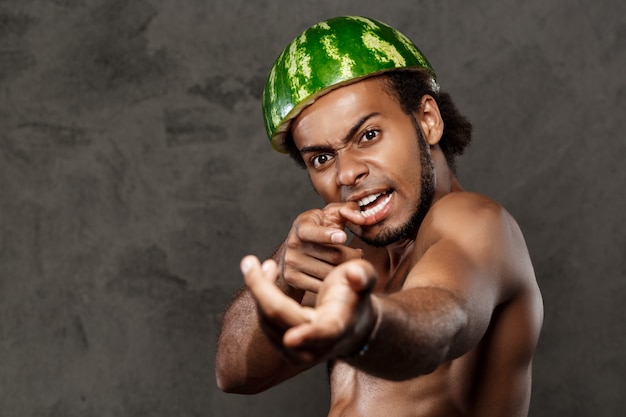 Homme africain avec la pastèque sur la tête dupe sur mur gris.