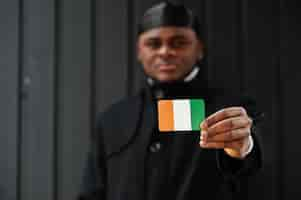 Photo gratuite un homme africain porte du durag noir tient le drapeau de la côte d'ivoire à la main isolé sur fond sombre