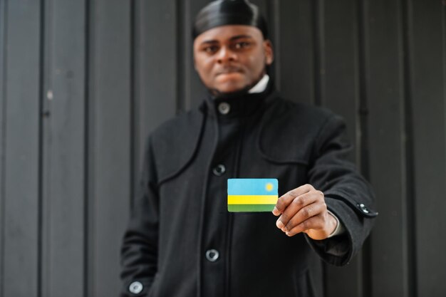 Un homme africain porte du durag noir tient le drapeau du Rwanda à la main isolé sur fond sombre