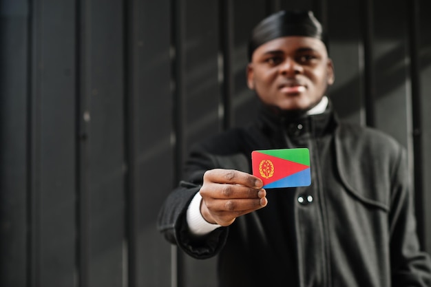 Un homme africain porte du durag noir tient le drapeau de l'Érythrée à la main isolé sur fond sombre