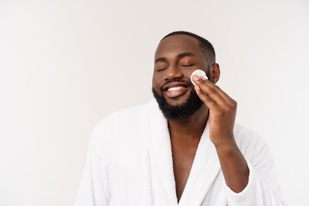 Un homme africain souriant applique le nettoyage de son concept de soins de la peau de l'homme du visage