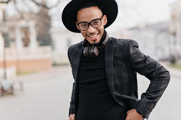 Homme africain souriant en pull noir posant. Mec spectaculaire en tenue décontractée profitant d'un week-end en ville.