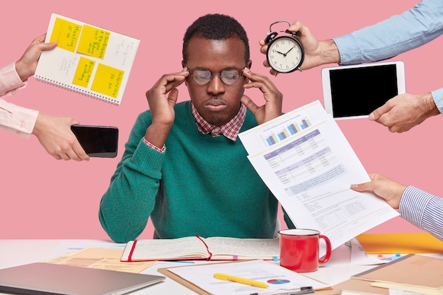 Photo gratuite homme afro-américain assis au bureau entouré de gadgets et de papiers