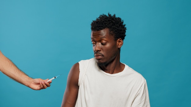 Homme afro-américain attendant de se faire vacciner en regardant la caméra. Personne noire se préparant au vaccin tiré des mains du médecin avec une seringue et une aiguille. Médecin vaccinant un adulte