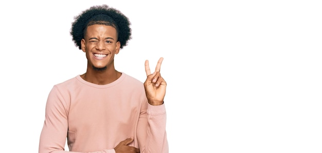 Photo gratuite homme afro-américain aux cheveux afro portant des vêtements décontractés souriant avec un visage heureux faisant un clin d'œil à la caméra faisant le signe de la victoire numéro deux