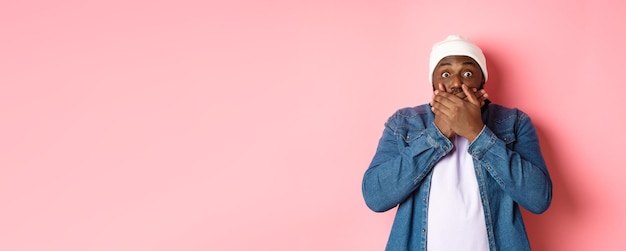 Photo gratuite un homme afro-américain choqué couvre la bouche et regarde la caméra debout sans voix contre le dos rose