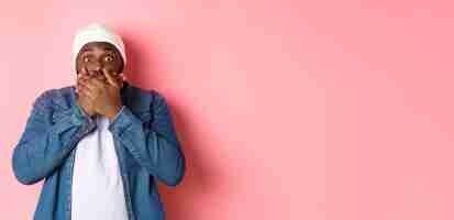 Photo gratuite un homme afro-américain choqué couvre la bouche et regarde la caméra debout sans voix contre le dos rose
