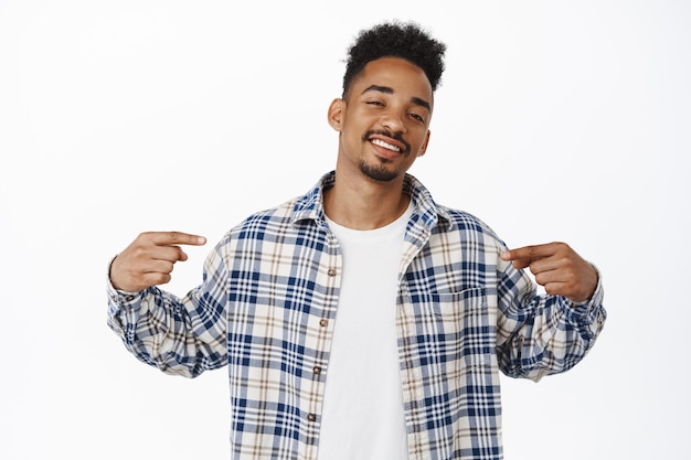 Un homme afro-américain cool et confiant présente le logo, pointant les doigts au centre avec un visage satisfait et satisfait, montrant une bannière publicitaire, debout sur fond blanc.