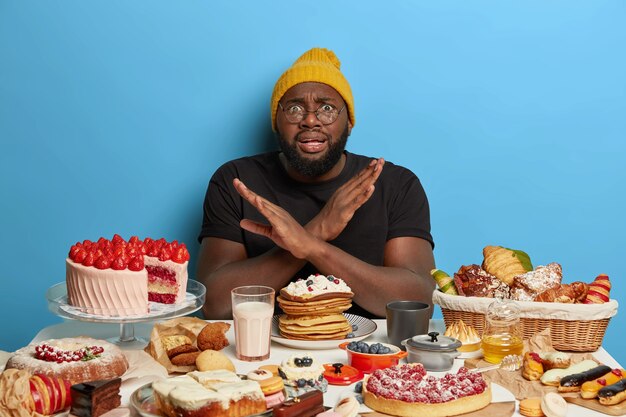 L'homme afro-américain croise les bras sur la poitrine, fait un geste de déni, refuse de manger des produits sucrés, s'assoit à table avec une boulangerie, continue de suivre un régime