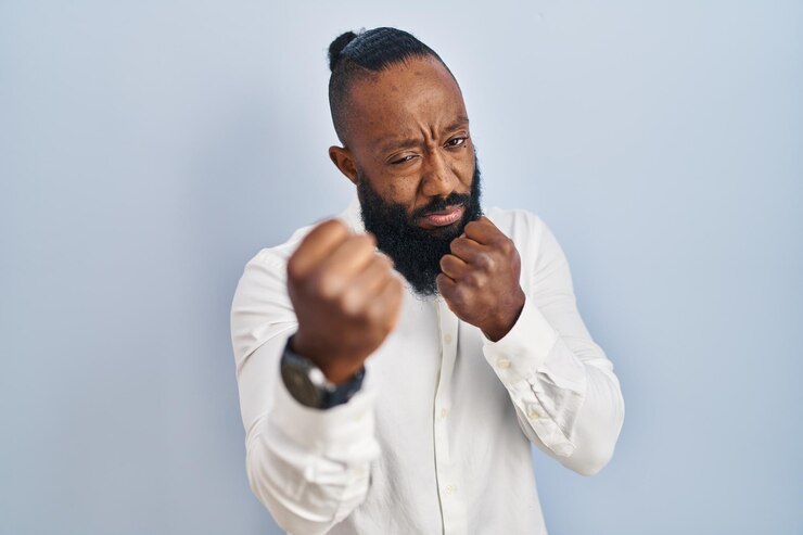 Photo gratuit homme afro-américain debout sur fond bleu prêt à se battre avec le geste de défense du poing visage en colère et bouleversé peur du problème