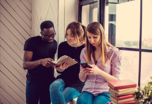 Homme afro-américain et deux femmes caucasiennes lisant un livre près de la fenêtre.