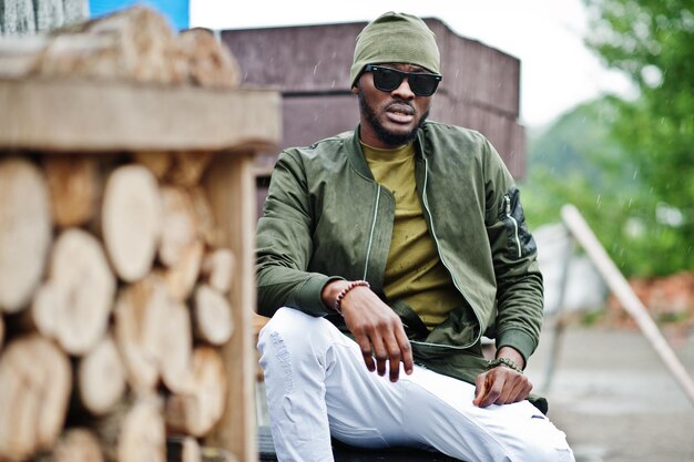 Homme afro-américain élégant en chapeau et lunettes de soleil posé en plein air sous la pluie