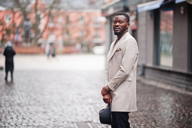 Un homme afro-américain élégant porte une veste beige et un chapeau noir pose dans la rue