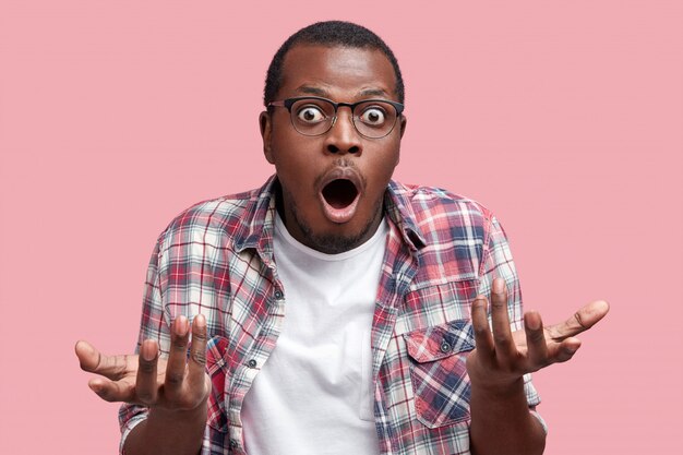Un homme afro-américain frustré se sent perplexe et hésitant, hausse les épaules perplexe, garde la bouche grande ouverte, ne sait pas quoi faire