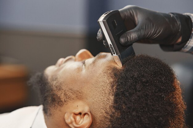 Homme afro-américain. Guy assis sur une chaise. Barber travaille avec une barbe.