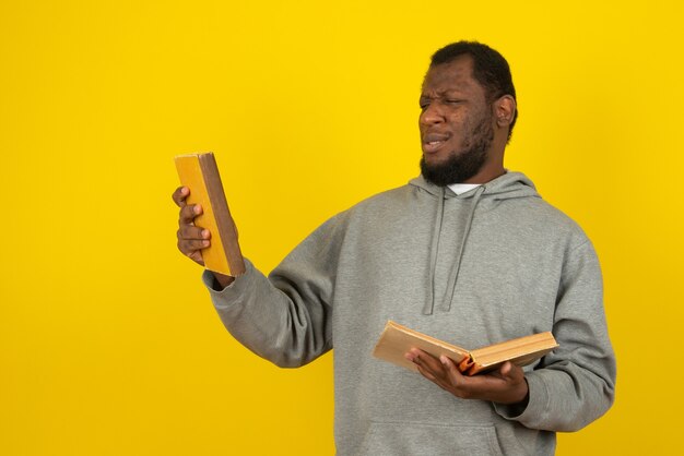 L'homme afro-américain jetant un coup d'œil au livre dans sa main, se dresse sur le mur jaune.