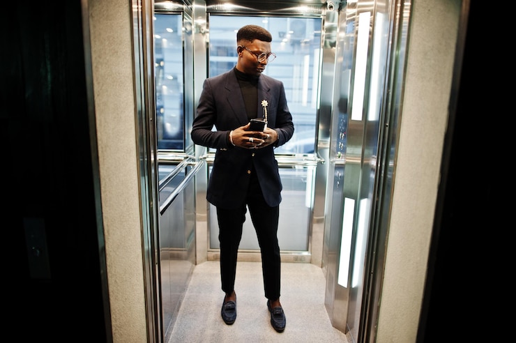 Photo gratuit homme afro-américain à la mode en costume et lunettes avec téléphone portable et tasse de café aux mains posées à l'intérieur de l'ascenseur