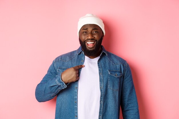 Un homme afro-américain offensé et confus se montrant lui-même, regardant la caméra dérangé, étant accusé, debout sur fond rose.