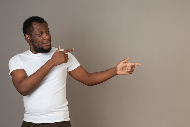 Photo gratuite l'homme afro-américain pointe à gauche avec ses doigts, debout devant le mur gris.