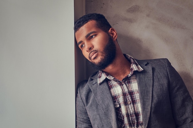 Photo gratuite un homme afro-américain portant une veste et une chemise à carreaux s'appuyant sur un mur et regardant ailleurs.