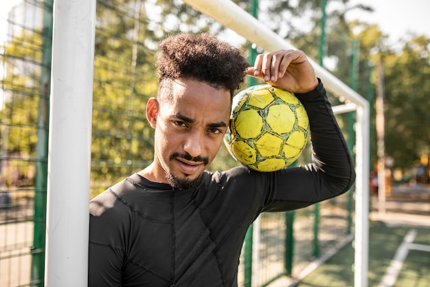 Homme afro-américain posant avec un ballon de foot sur un terrain