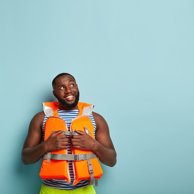 Photo gratuite homme afro-américain positif heureux d'avoir une belle croisière divertissante, porte un gilet de sauvetage orange