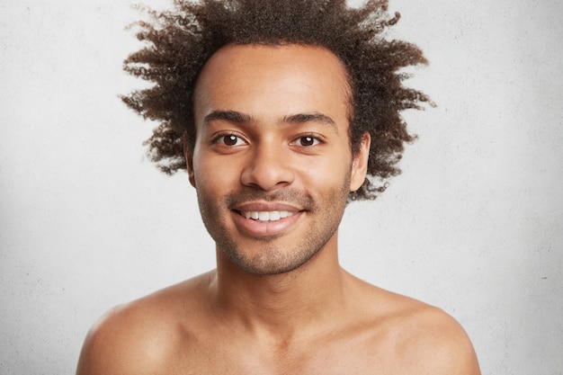 Photo gratuite homme afro-américain positif nu avec une peau sombre et saine et des cheveux bouclés, sourit doucement