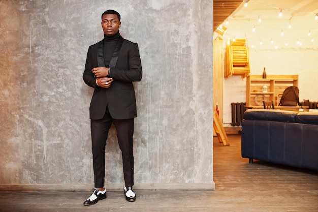 Photo gratuite homme afro-américain puissant et fort en costume noir et col roulé posant contre un mur gris