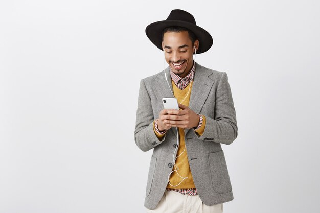 Homme afro-américain de Stlylish en costume à l'aide de smartphone et écouter de la musique dans des écouteurs