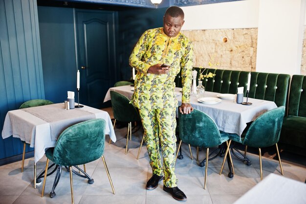 Homme afro amical en vêtements jaunes traditionnels au restaurant faisant un appel téléphonique en attendant quelqu'un