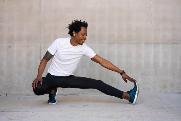 Homme afro athlétique étirant ses jambes et s'échauffer avant de faire de l'exercice à l'extérieur. Concept de sport et de mode de vie sain.