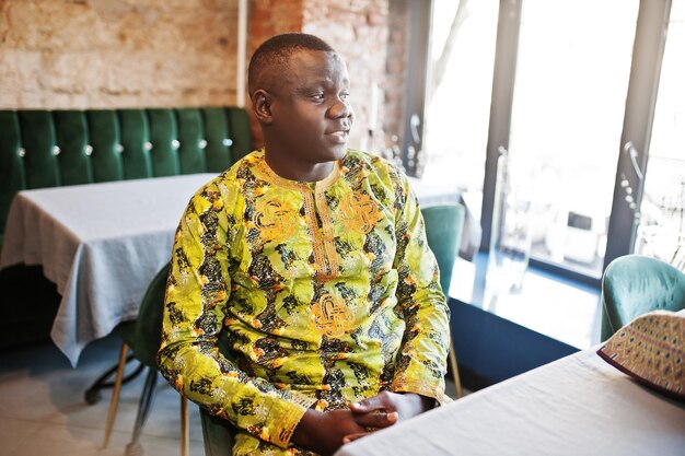 Homme afro sympathique en vêtements jaunes traditionnels assis au restaurant