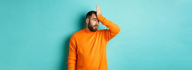 Photo gratuite l'homme agacé roule des yeux et fait facepalm debout sur fond turquoise