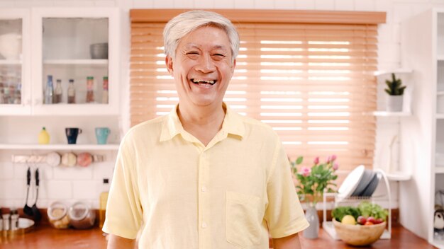 Homme âgé asiatique se sentir heureux en souriant et en regardant vers la caméra tout en se détendre dans la cuisine à la maison.