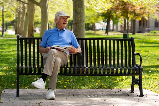 Homme âgé assis sur un banc à l'extérieur et lisant un livre