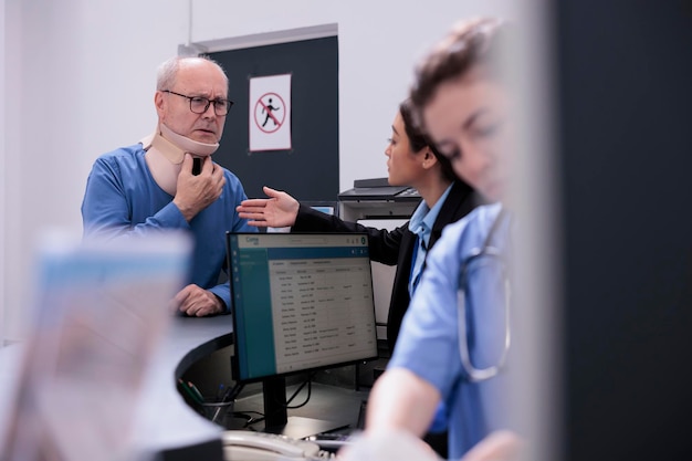 Photo gratuite homme âgé avec collier cervical souffrant de douleur après un accident demandant de l'aide à la réceptionniste lors de la consultation de visite de contrôle au comptoir de l'hôpital. service et concept de soutien aux soins de santé