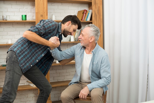 Homme âgé et jeune homme heureux avec les mains jointes dans la chambre