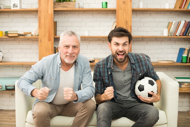 Homme âgé et jeune homme qui pleure avec ballon en regardant la télévision sur un canapé