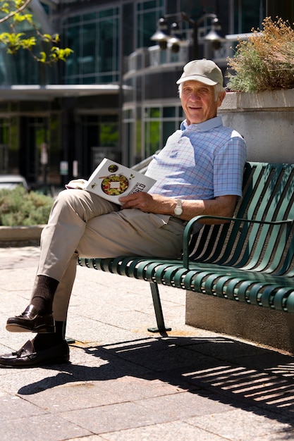 Homme âgé lisant un livre sur un banc à l'extérieur