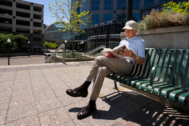 Homme âgé lisant un livre sur un banc à l'extérieur